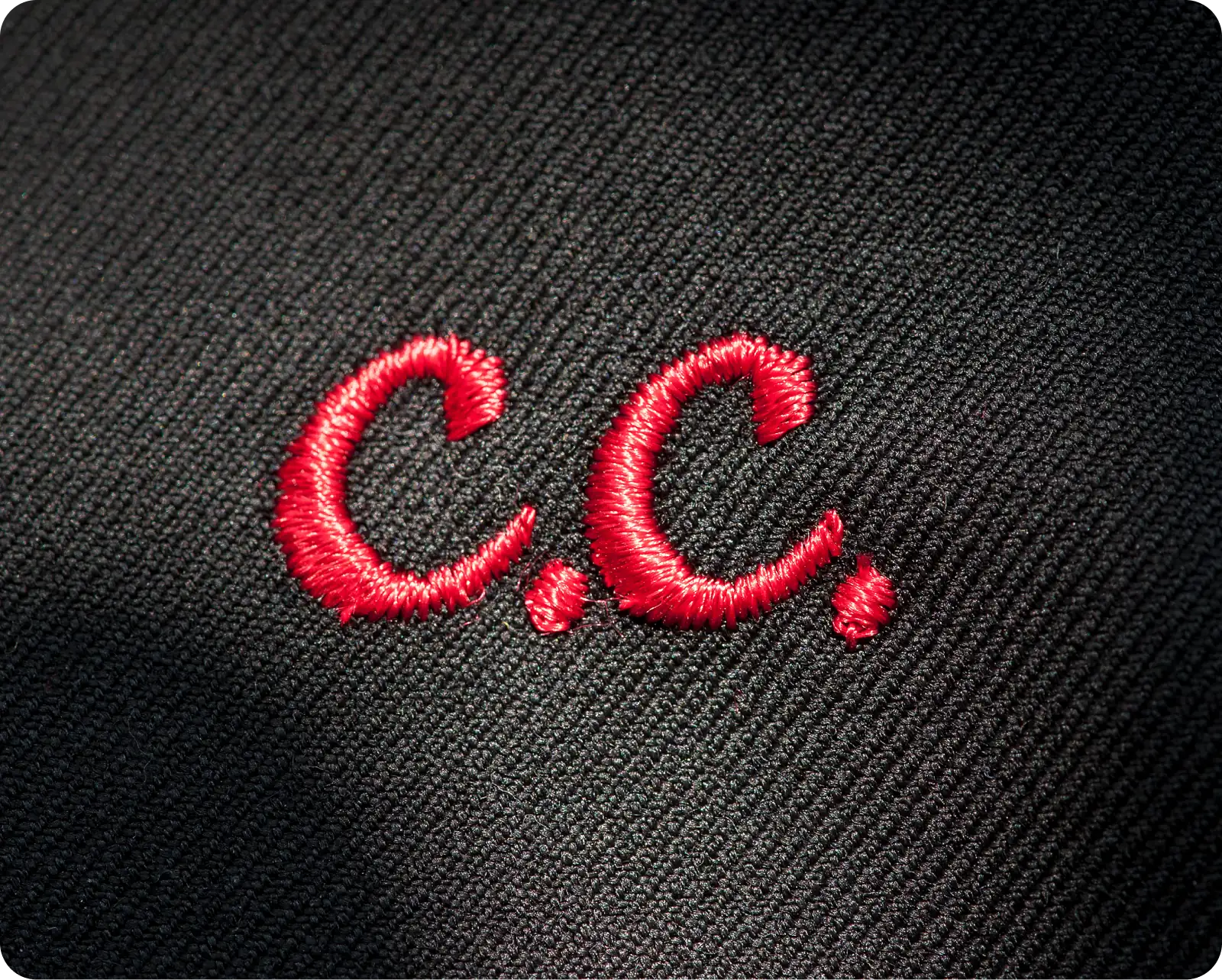 Red embroidered initials "C.C." on black fabric background.