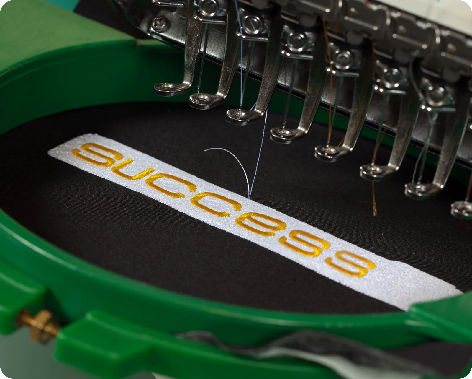 Machine embroidery in progress, stitching the word "success" in yellow thread on black fabric.